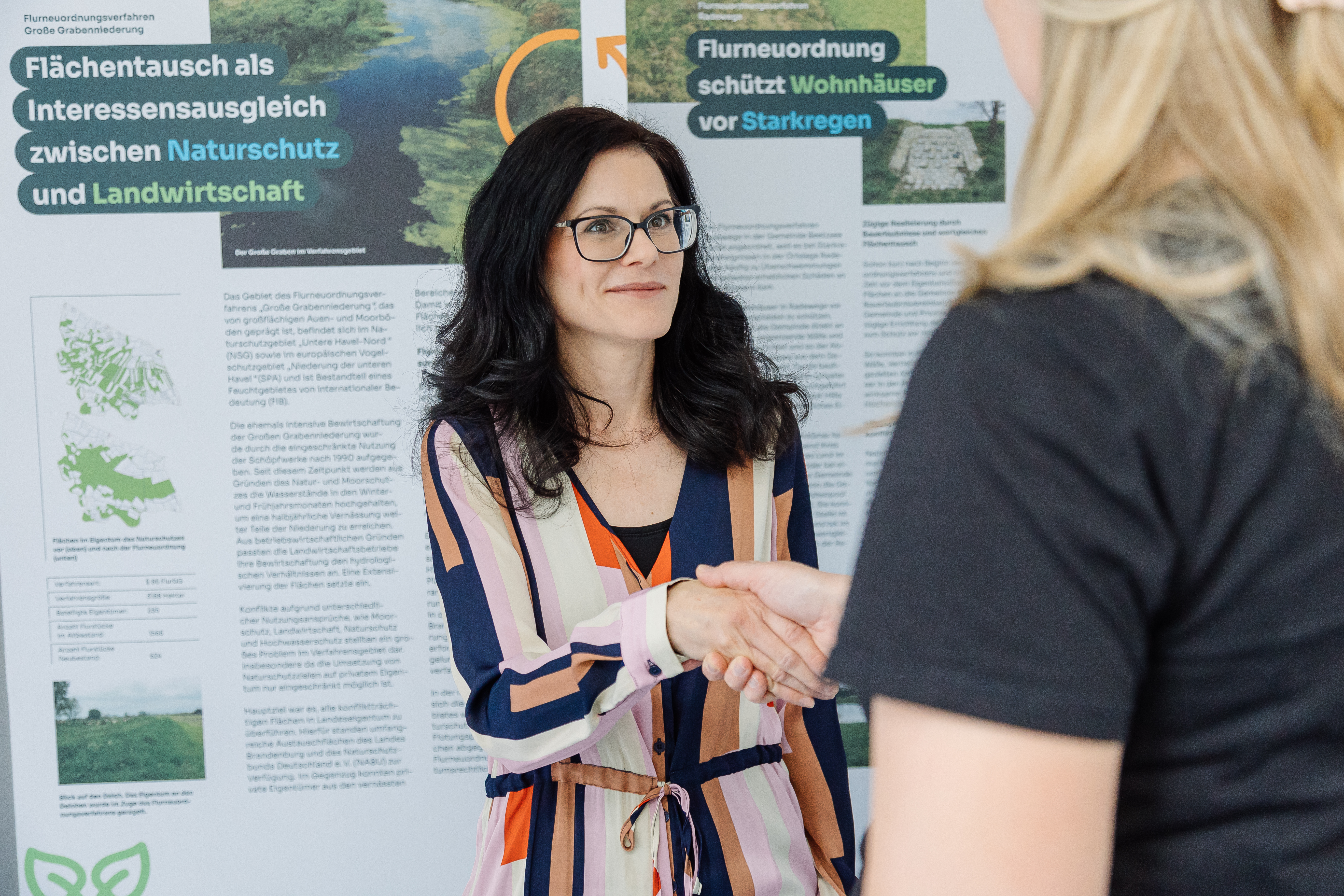 2 Menschen, dass die Hände schütteln vor eine Infotafel